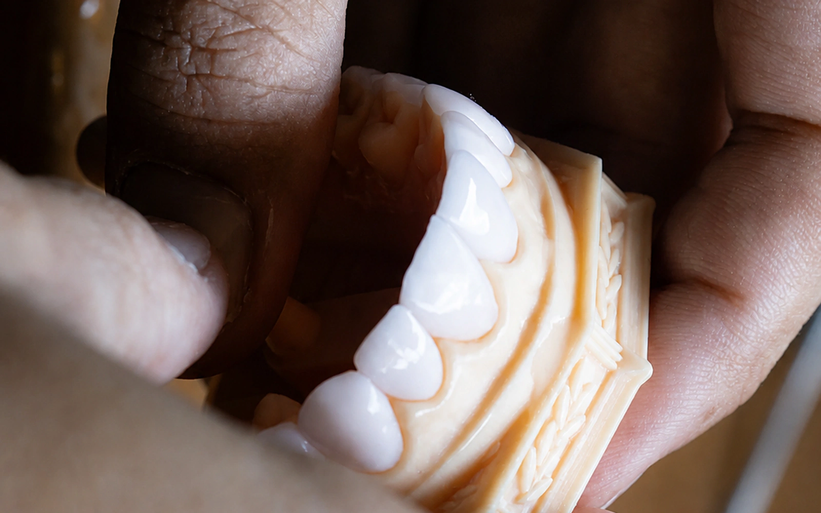 Mãos examinando o acabamento de uma prótese odontológica no laboratório Brunetti
