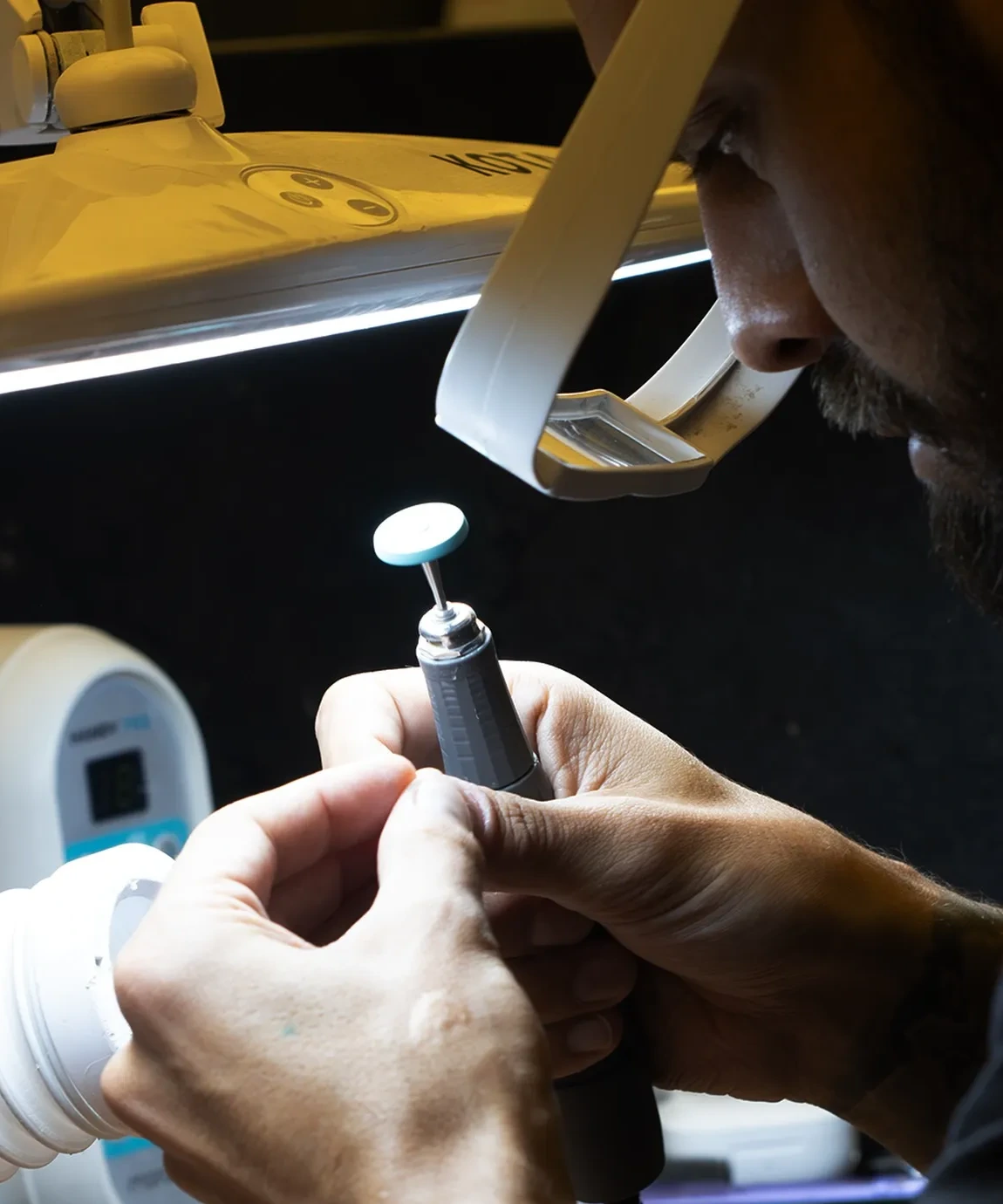 Técnico do laboratório Brunetti dando acabamento a uma peça de cerâmica sob lupa iluminada